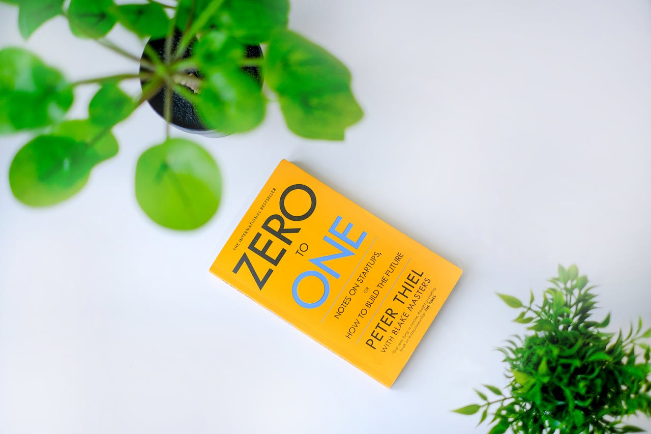 gallery-06 Top view of 'Zero to One' book surrounded by green plants on a white backdrop, providing ample copy space.
